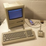 Mac Plus 1MB, powerd up, on desk with FloppyEmu Boot Device